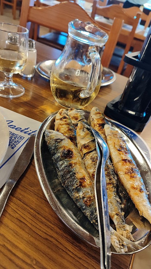 Gegrillte Sardinen und ein Krug prickelnd grüner Wein